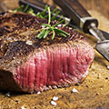 Ein angebratenes rotes Stück Fleisch medium rare liegt auf braunem Untergrund mit einem Messer