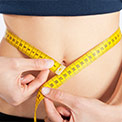 Bauch einer Frau, von einem gelben Maßband umschlungen