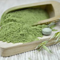 Grünes feines Chlorella Pulver in einem großen Holzlöffel und auf einem Holzbrett