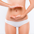 Bauch und Oberschenkel einer schlanken Frau in weißer Unterwäsche, die ihre Hände ober- und unterhalb des Bauchnabels hält