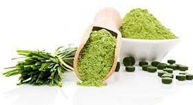 Grünes Pulver in einer Schale und einer Schaufel, daneben grüne Tabletten und Chlorella Stiele Grünes Pulver in einer Schale und einer Schaufel, daneben grüne Tabletten und Chlorella Stiele