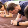 Männer und Frauen in violetten Shirts die gleichzeitig die Plank Position halten