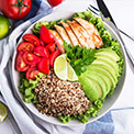 Weiße Schüssel mit Avocado, Hühnerfleisch, Quinoa, Tomaten und Salat auf einem weiß-blauen Geschirrtuch Weiße Schüssel mit Avocado, Hühnerfleisch, Quinoa, Tomaten und Salat auf einem weiß-blauen Geschirrtuch