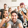 Ein Mann macht ein Selfie von mehreren Frauen und einem Mann in Sportklamotten und mit Hanteln