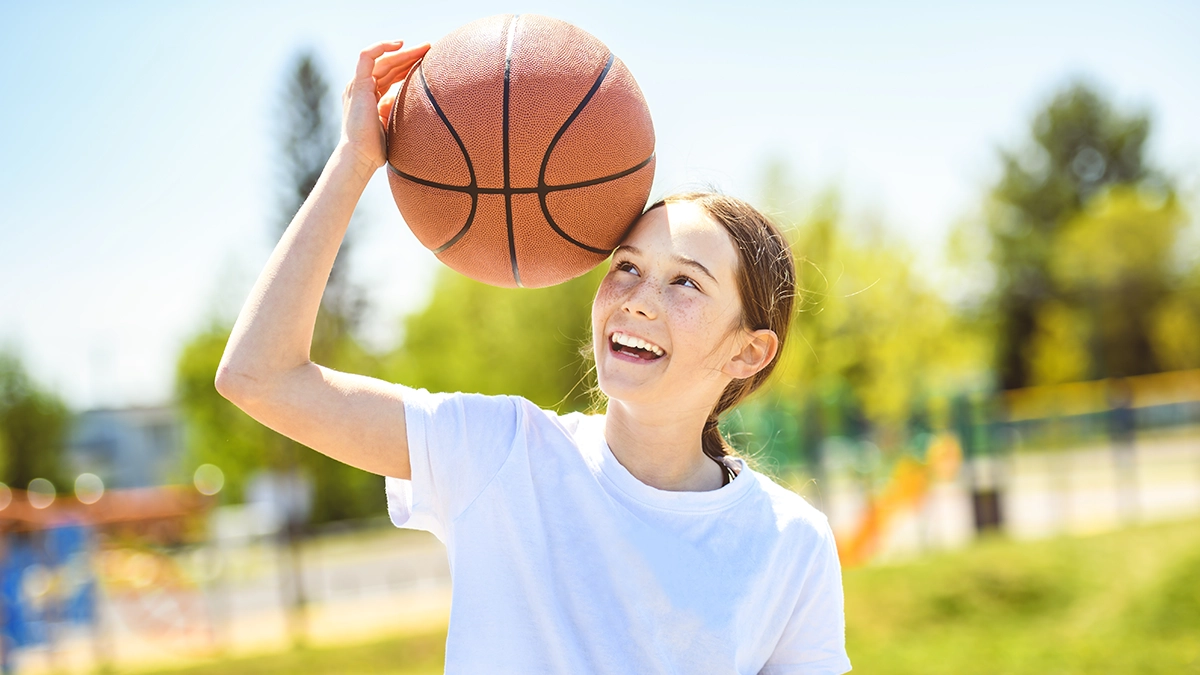 Ein Portrait eines kleinen Mädchens, das mit einem Basketball im Park spielt