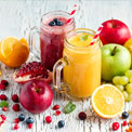 Zwei durchsichtige Smoothiegläser mit rotem und gelbem Smoothie auf hölzernem Untergrund von bunten Früchten umgeben